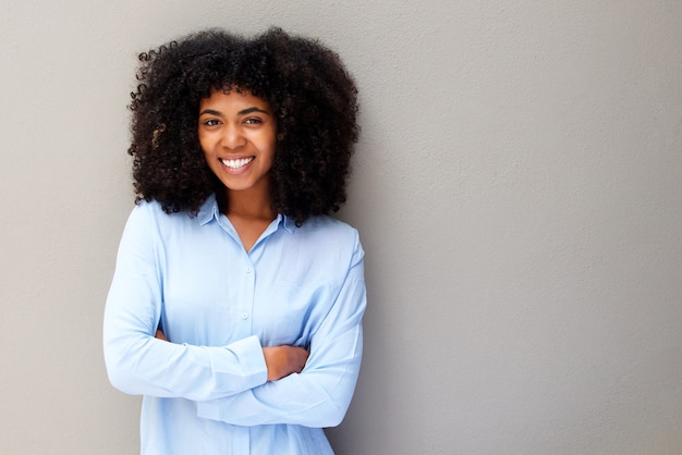happy young african american woman smiling against gray background with arms crossed