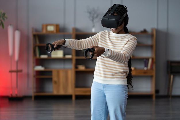 Happy young african american woman wearing virtual reality goggles playing video games at home