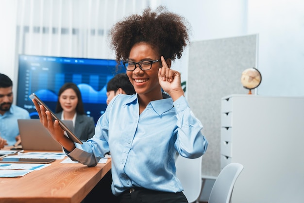 Happy young african businesswoman wearing glasses portrait with group of office worker on meeting with screen display business dashboard in background Confident office lady at team meeting Concord