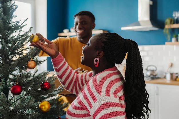 Photo happy young african couple enjoying fun time while decorating christmas tree at home together