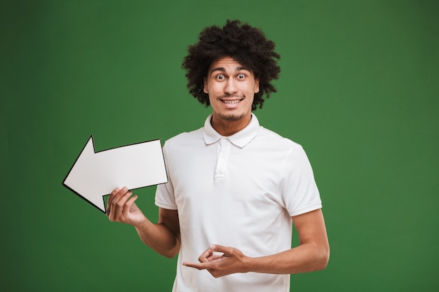 Happy young african curly man holding arrow pointing.