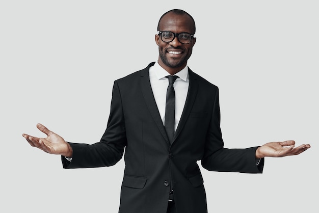 Happy young African man in formalwear looking at camera and smiling while standing against grey wall