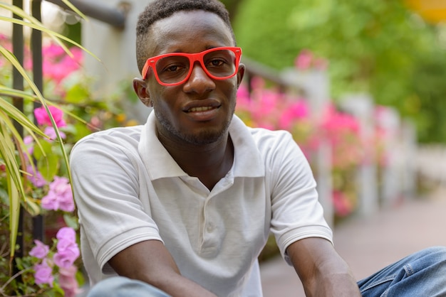 Happy young African man with eyeglasses smiling and sitting at the park outdoors