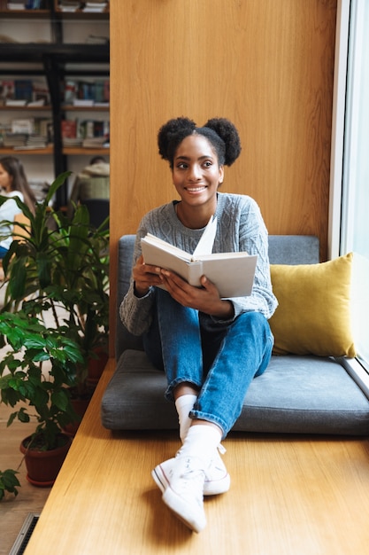 Happy young african student girl studying at the library, reading a book