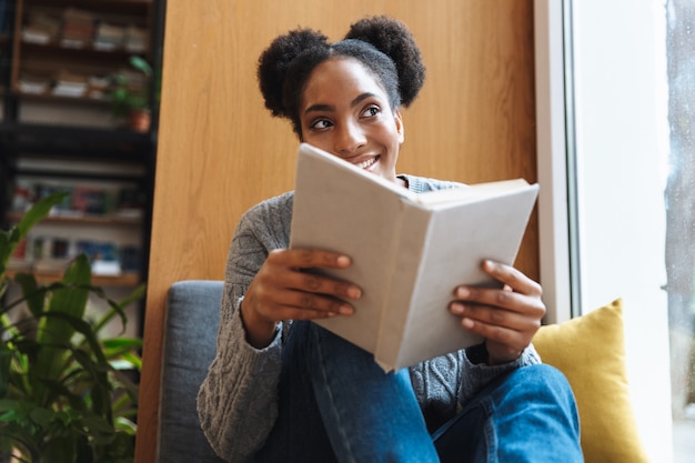 Счастливый молодой африканский студент девушка учится в библиотеке, читая книгу