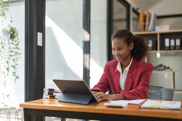 행복한 젊은 아프리카계 미국인 기업가 여성이 재정적 성공을 즐기는 혜택을 분석하는 랩톱 컴퓨터에서 계산기로 이익을 세고 있습니다.