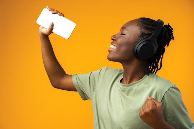 Happy young afro american woman listening to music in headphones against yellow background