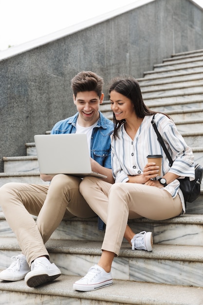 happy young amazing loving couple business people colleagues outdoors outside on steps using laptop computer drinking coffee.