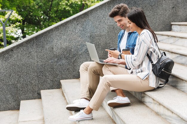 happy young amazing loving couple business people colleagues outdoors outside on steps using laptop computer drinking coffee.