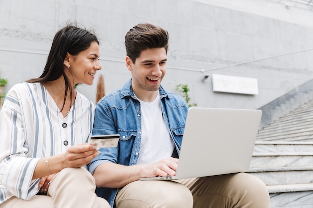 happy young amazing loving couple business people colleagues outdoors outside using laptop computer holding credit card.