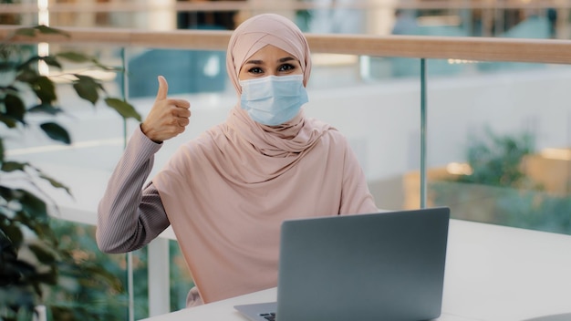 Happy young arab businesswoman sitting at office desk typing on laptop working on internet checking