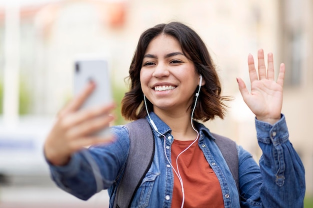 屋外に立っている間、携帯電話を介してビデオ通話を行う幸せな若いアラブ女性