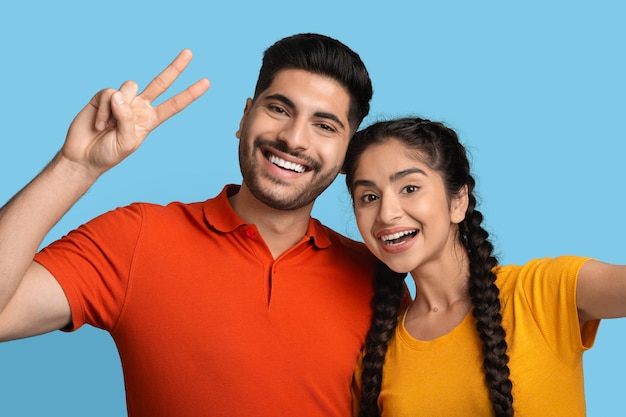 Happy young arabic couple taking selfie together over blue background