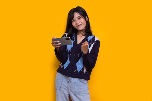 happy young asian beautiful woman using mobile phone isolated on yellow background