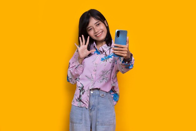 happy young asian beautiful woman using mobile phone isolated on yellow background