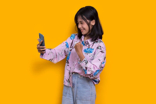 happy young asian beautiful woman using mobile phone isolated on yellow background