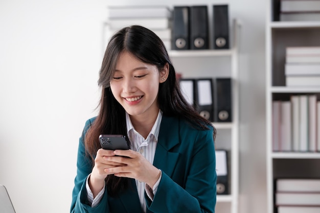 Happy young Asian business woman with a smile using smartphone at the office