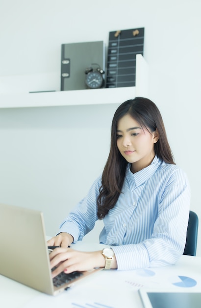 Happy young asian business woman working on her laptop at workplace.