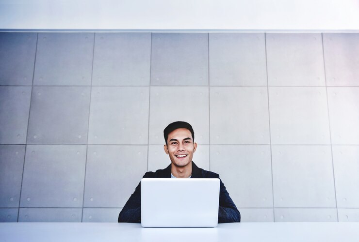 Happy Young Asian Businessman Working on Computer Laptop in his Workplace
