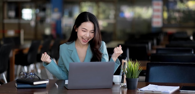 Happy young asian businesswoman sitting on her workplace in the office. Young woman working at laptop in the office.