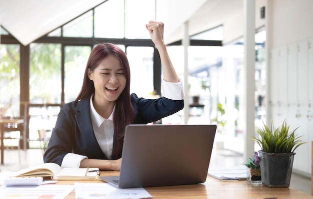 사무실에서 그녀의 직장에 앉아 행복 한 젊은 아시아 사업가 사무실에서 노트북에서 일하는 젊은 여자