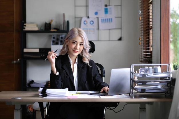 Счастливая молодая азиатская деловая женщина, работающая на клавиатуре ноутбука с документом в офисе