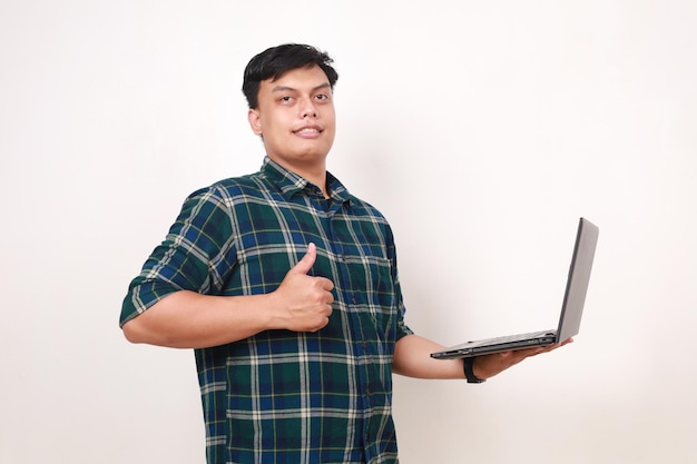 Счастливый молодой азиатский студент, держащий ноутбук, показывая большой палец, изолированный на белом