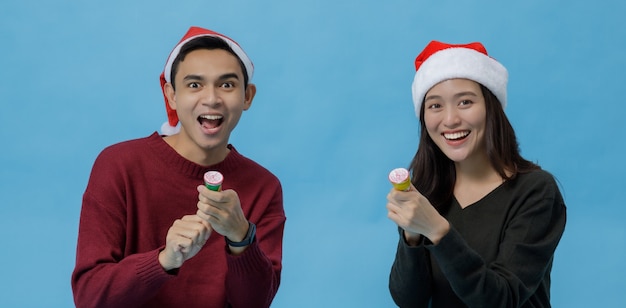 행복한 젊은 아시아 커플이 스튜디오 촬영에서 파란색 배경에 격리된 행복한 웃는 얼굴로 종이 플레어를 들고 있습니다. 연인 개념의 크리스마스 축하입니다.