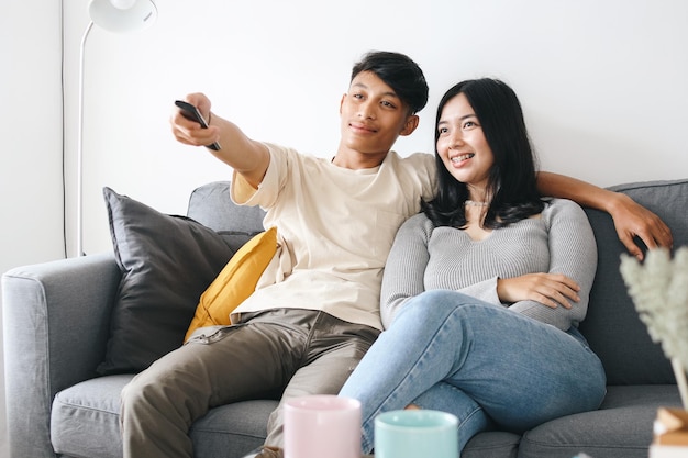 Happy young Asian couple relaxing and watching TV at home