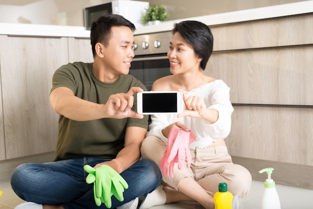 Happy young Asian couple showing smartphone while cleaning house