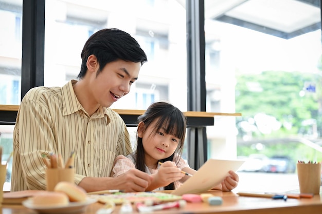 幸せな若いアジアの娘は、父親と一緒に絵のワークショップを楽しんでいます