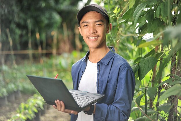 Happy of young Asian farmer man smiling when checking the long beans quality using laptop