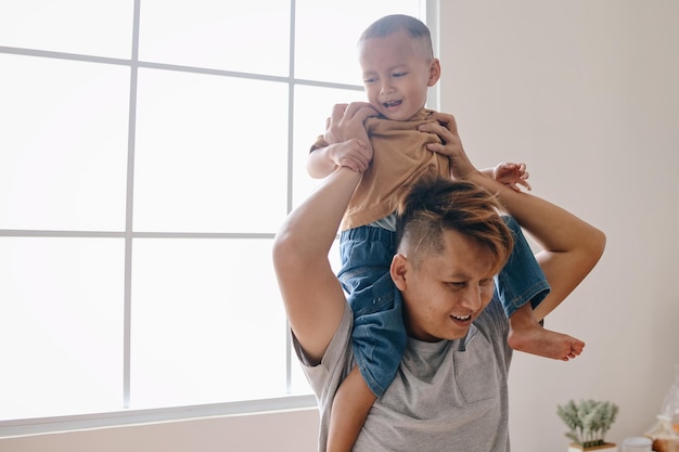 Happy young Asian father giving his kid piggyback ride on shoulders Father and son spending time to