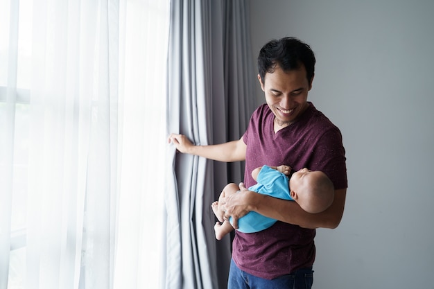 Happy young asian father holding his newborn sweet adorable baby sleeping on his arms while at home