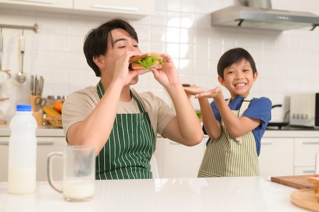 집에서 부엌에서 건강한 음식을 먹는 행복한 젊은 아시아 아버지와 아들