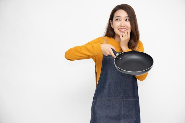 Happy young Asian female housewife wearing kitchen apron cooking and holding pan isolated on white background
