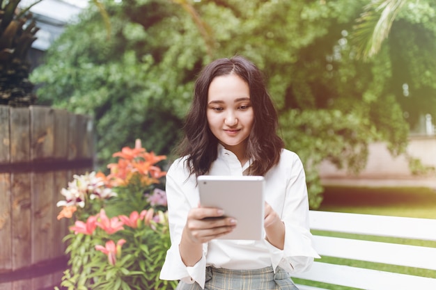 Happy young asian female student in a park working on laptop