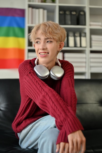 A happy young Asian gay man sits on a sofa in his modern living room LGBTQ