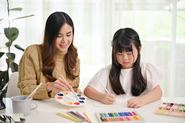 Happy young Asian girl drawing and painting with water colors with her mom