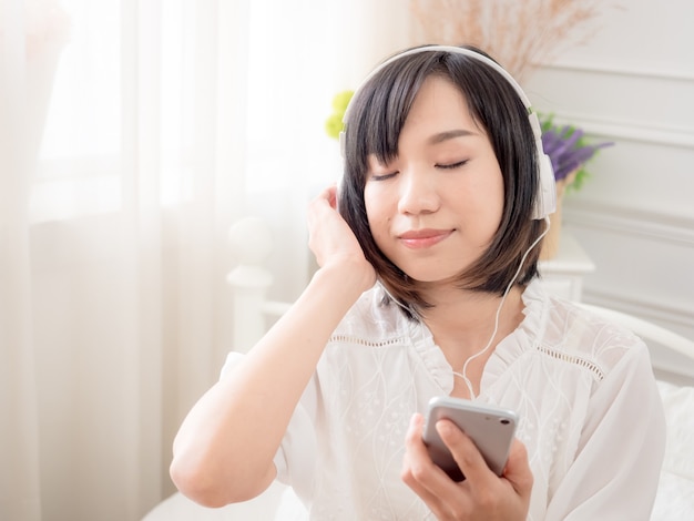 Felice giovane ragazza asiatica che ascolta la musica sul letto