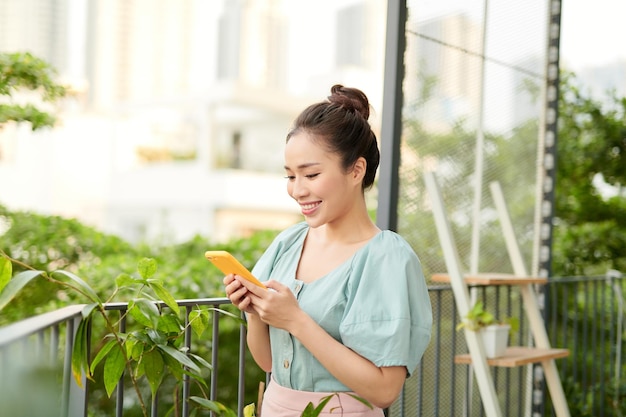 Felice giovane ragazza asiatica che parla al telefono quando si è in piedi sul balcone