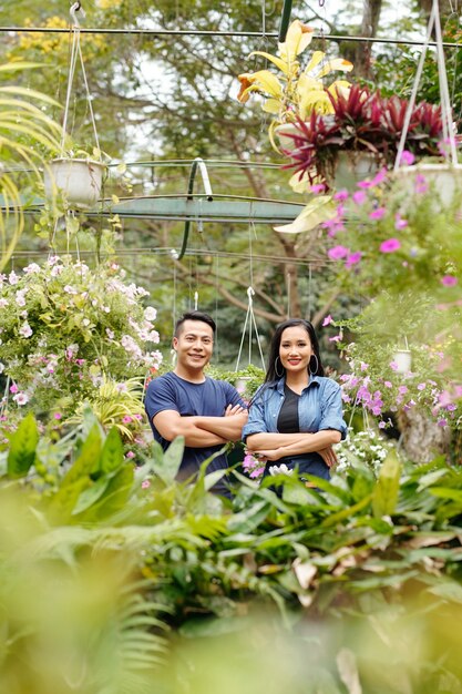 Happy young Asian greenhouse owners standing in greenhouse with plants and flowers around