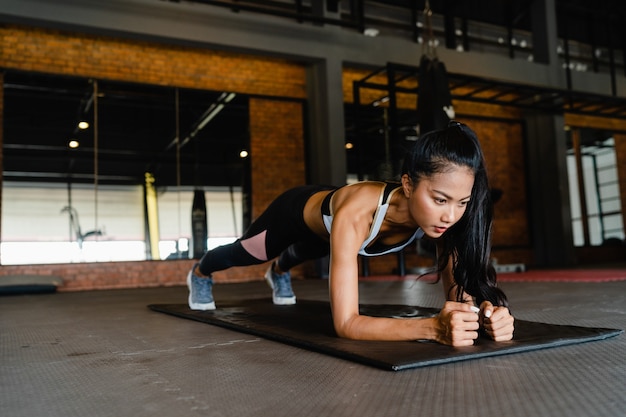 Happy young asian lady doing plank fat burning workout in fitness class