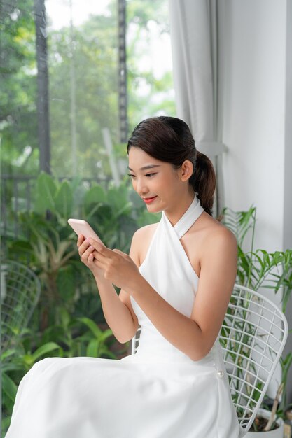 Happy Young Asian Lady Using Modern Smartphone While Resting At Home