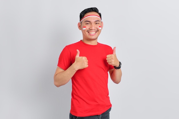 Счастливый молодой азиатский мужчина празднует День независимости Индонезии, показывая большой палец вверх жестом на белом фоне