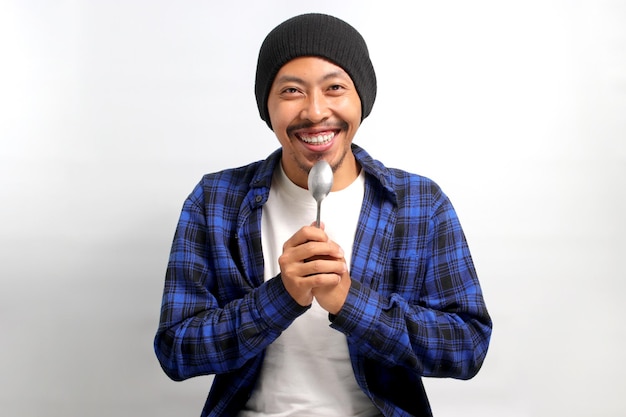 Photo happy young asian man holding spoon near his mouth feeling excited to eat