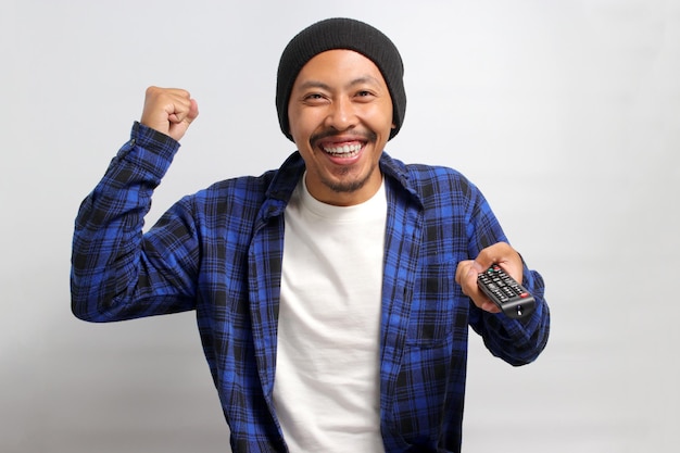 Happy young Asian man holding a TV remote while watching a movie isolated on a white background