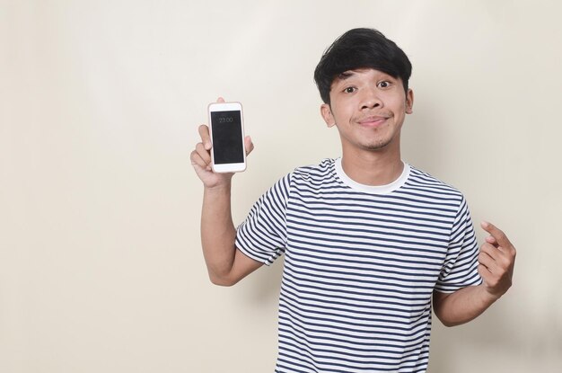 Happy young asian man wearing striped tshirt holding smartphone and pointing at mobile screen