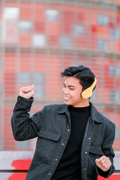 Happy young asian man with headphones dancing on city street