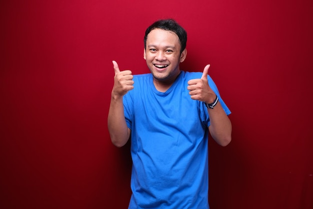 Счастливый молодой азиатский мужчина с улыбающимся лицом и большими пальцами руки вверх или знаком "ок"